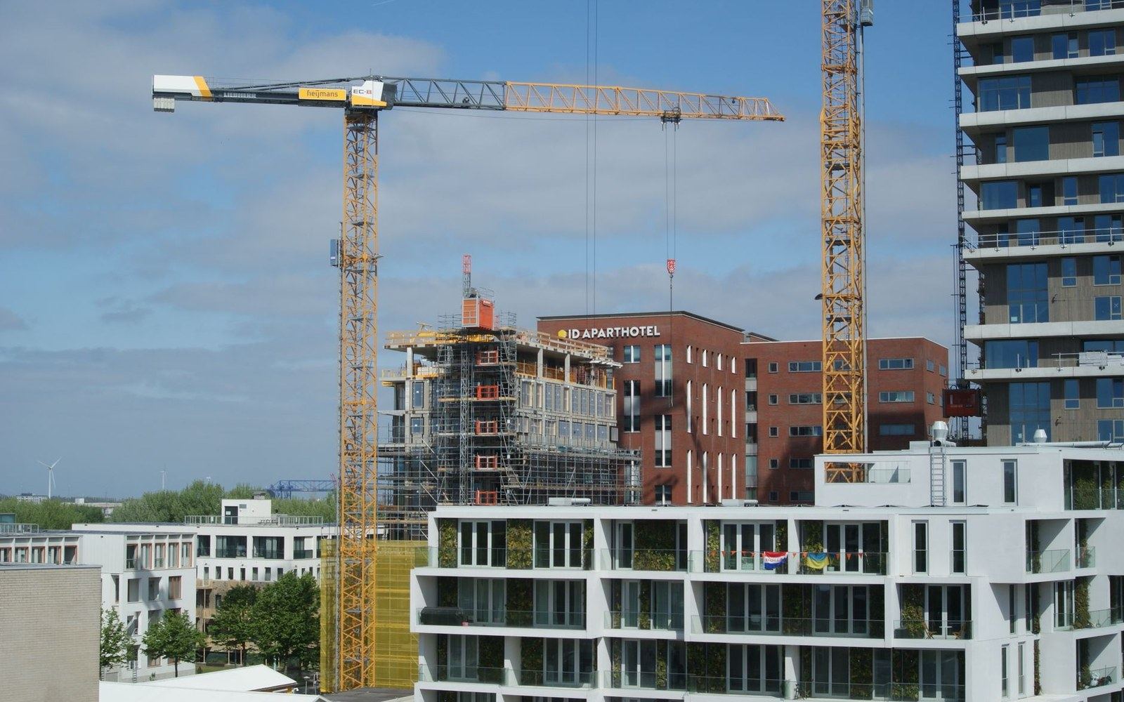 Construction cranes tower over apartment buildings and the ID Aparthotel under scaffolding