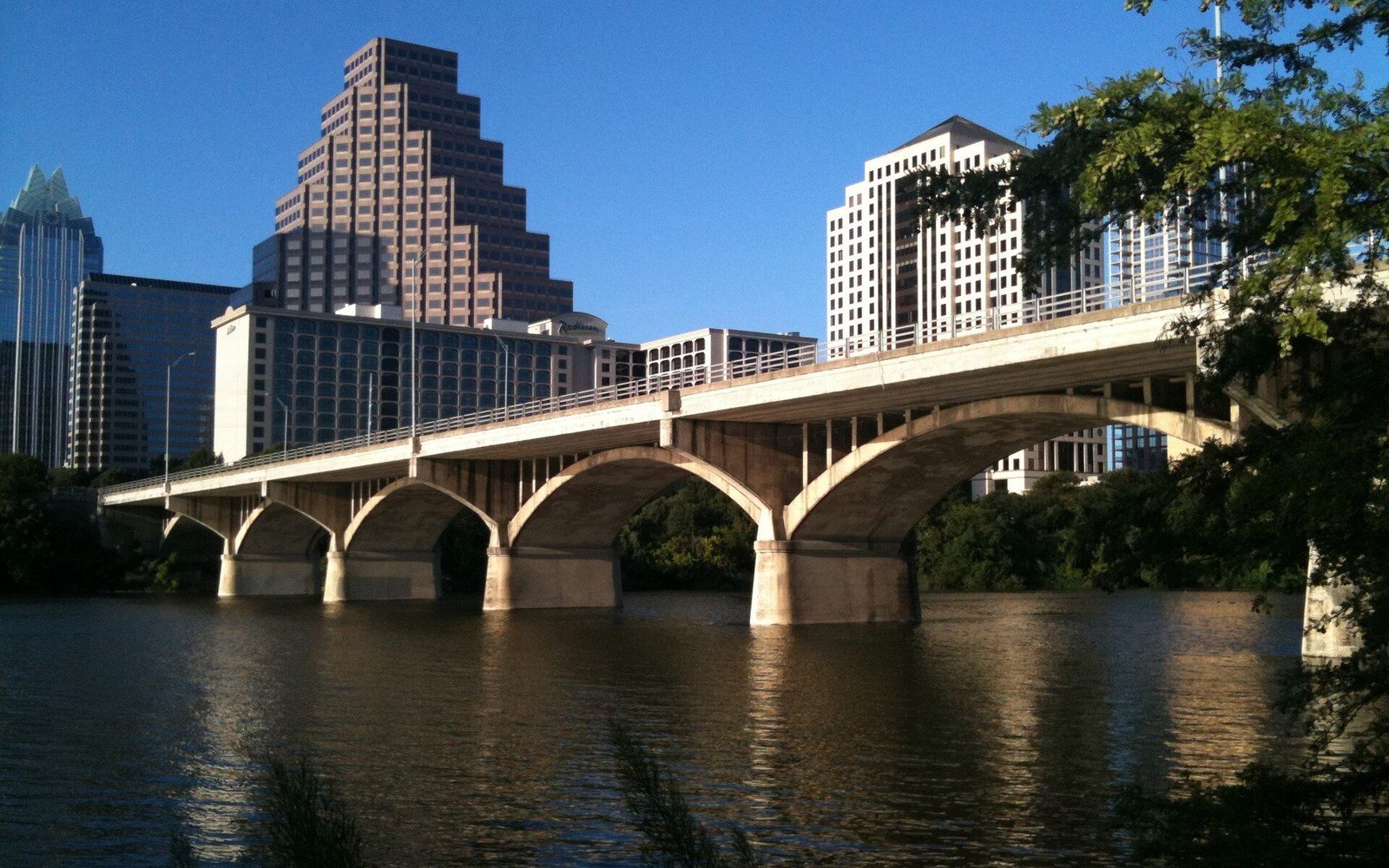 Arched stone bridge spans a river with downtown Austin's skyline behind it