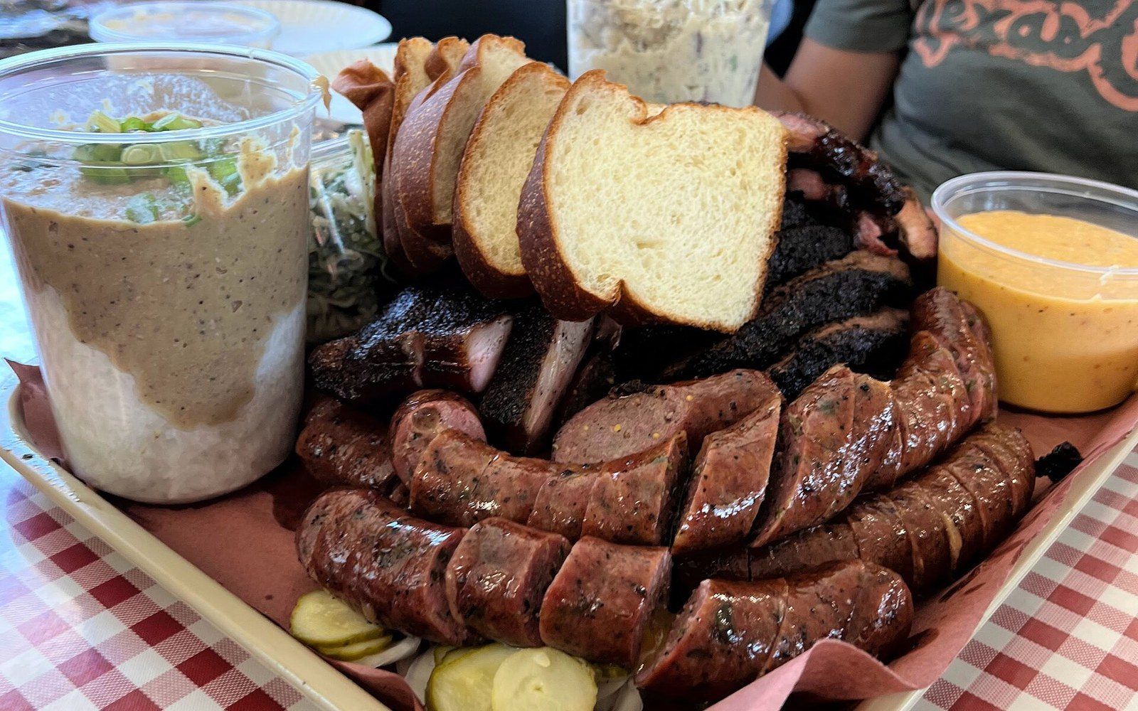 Barbecue platter with sliced brisket, smoked sausage links, white bread and pickles