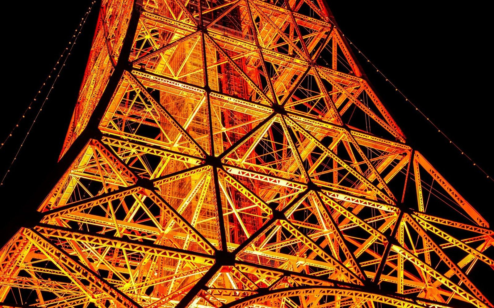 Latticed steel girders of a lit tower form triangular patterns against a night sky