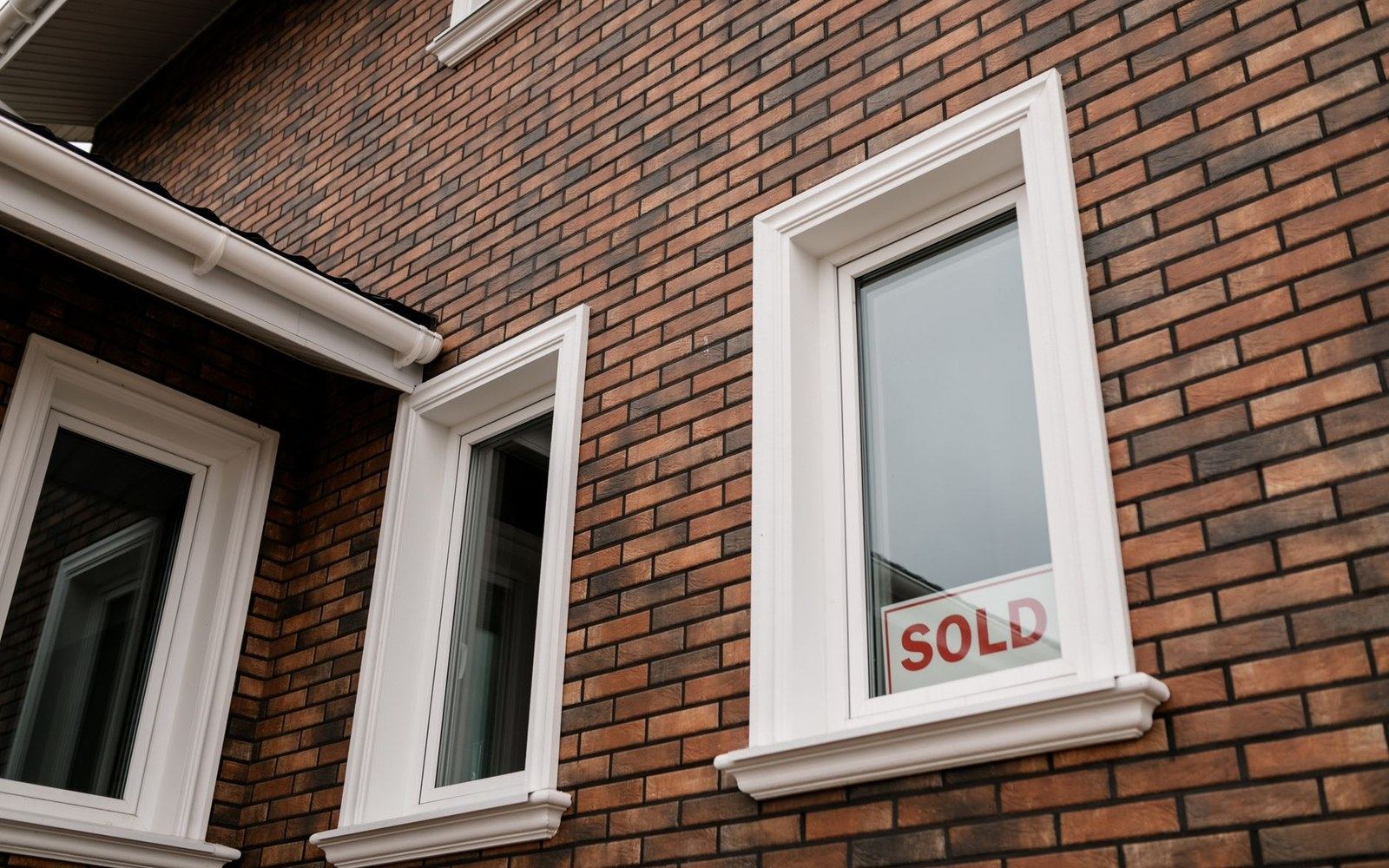A "sold" sign displayed in the window of a brick house with white trim