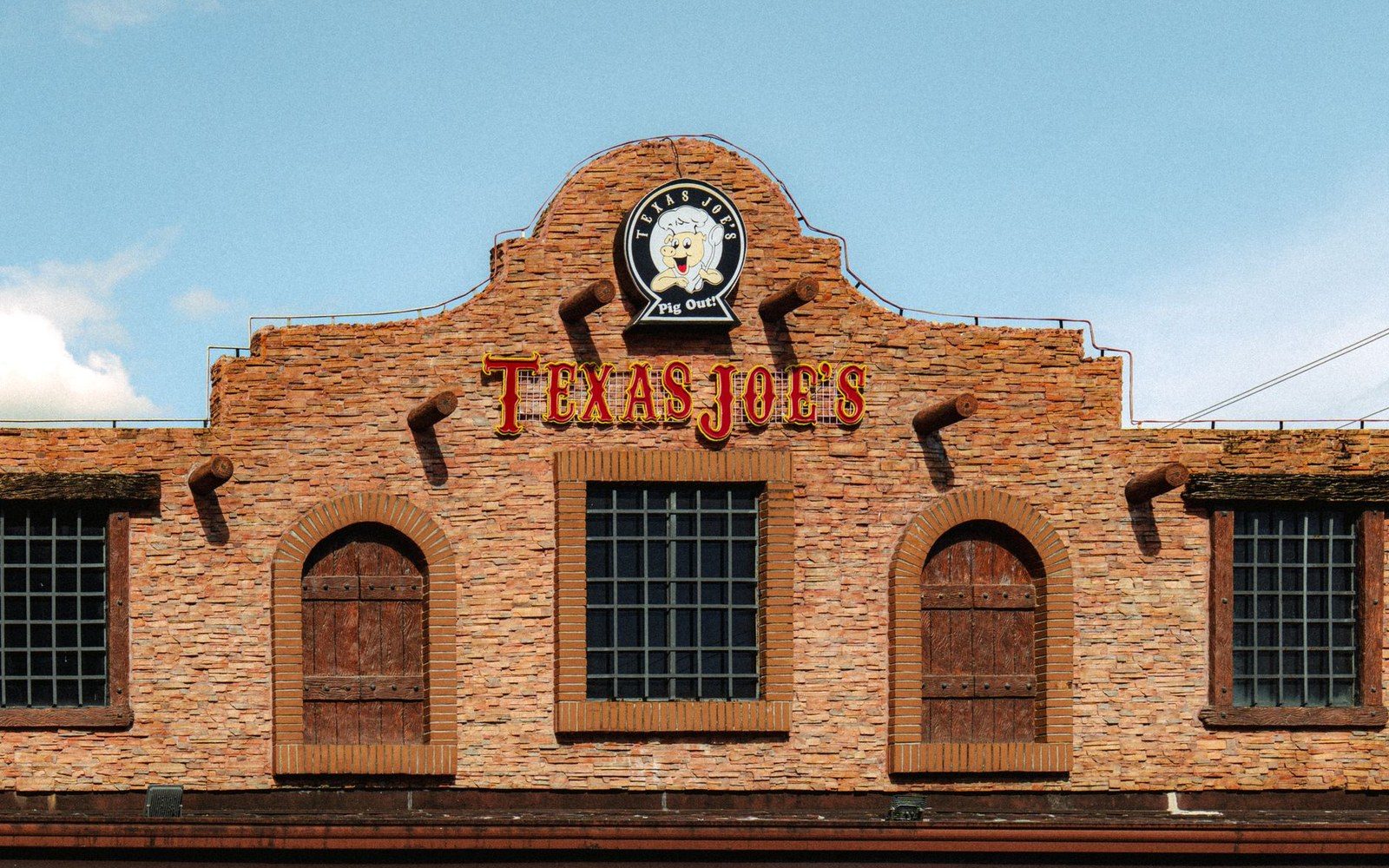 Brick facade of Texas Joe's restaurant with arched wooden doors and a circular sign